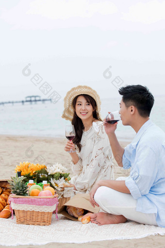 浪漫的青年夫妇坐在沙滩上喝红酒女朋友高端摄影图