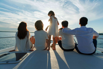 夕阳下坐在游艇上的快乐一家人背影氛围照片