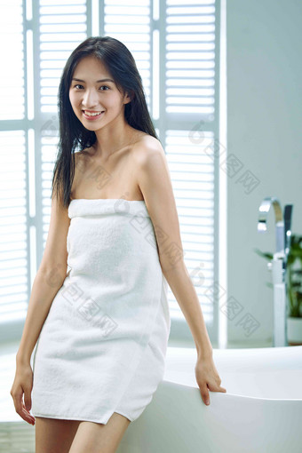 裹着浴巾的青年女人站在浴缸旁