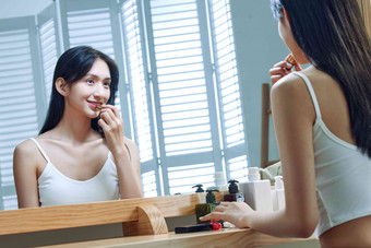 漂亮的年轻女人照着镜子涂口红