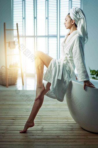 身穿浴袍的青年女人坐在浴缸边