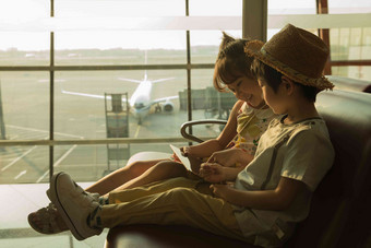 两个小朋友坐在机场候车厅看平板电脑