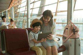 年轻妈妈和儿子在机场候机厅看平板电脑青年女人相片