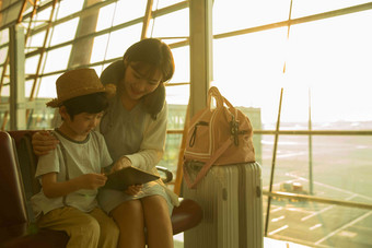年轻妈妈和儿子在机场候机厅看平板电脑