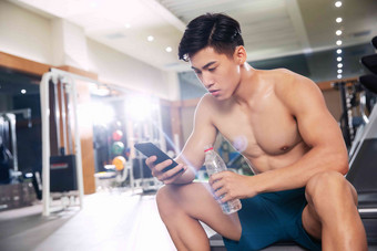 青年男人在健身房里喝水<strong>手机</strong>高清照片