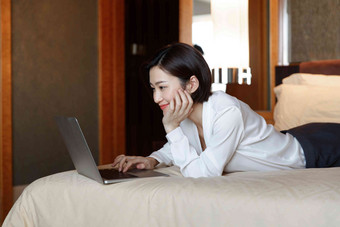 年轻女人趴在床上用电脑