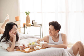 快乐的年轻情侣在床上吃早餐浪漫高端镜头