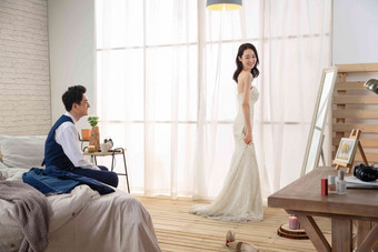 卧室里新婚的丈夫欣赏妻子穿婚纱的样子婚纱照片
