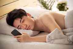 躺在床上玩手机的年轻男人