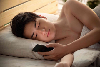 <strong>躺在床上</strong>玩手机的年轻男人皮肤写实镜头
