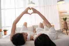 快乐的年轻情侣躺在床上做心形手势做手势清晰照片