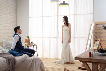 年轻丈夫坐在床上欣赏妻子穿婚纱的样子