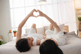 快乐的年轻情侣躺在床上做心形手势享乐摄影图