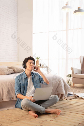 年轻的男青年坐在<strong>地板</strong>上使用笔记本电脑