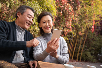 老年夫妇在庭院使用手机坐着高质量摄影图