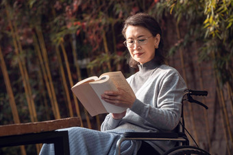 户外老年女人坐在轮椅上看书
