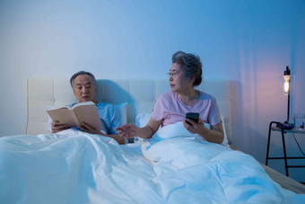 老年夫妇坐在床上<strong>看书</strong>看手机
