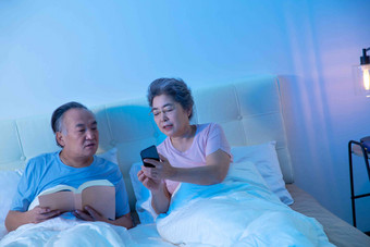 老年夫妇坐在床上看手机老年伴侣场景