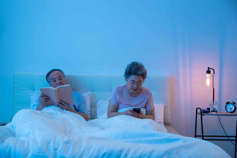 老年夫妇坐在床上看书看手机