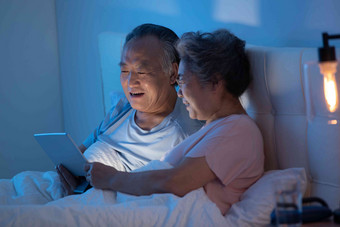 老年夫妇坐在床上用平板电脑看视频视频聊天氛围素材