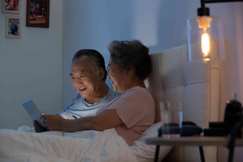 老年夫妇坐在床上用平板电脑看视频电脑镜头