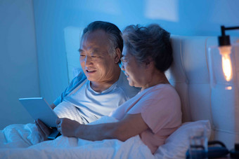 老年夫妇坐在床上用平板电脑看视频
