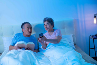 老年夫妇坐在床上看手机