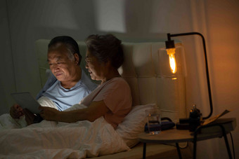 老年夫妇坐在床上用平板电脑看视频