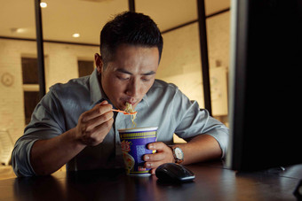 在办公室加班吃方便面的青年男人吃饭高清摄影图