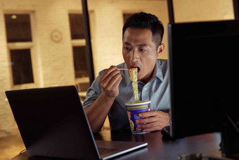 在办公室加班吃<strong>方便面</strong>的青年男人使用电脑高端摄影
