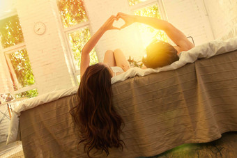 快乐的年轻情侣躺在床上做心形手势帅哥氛围素材