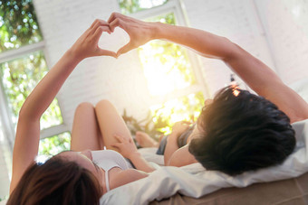 幸福的年轻伴侣躺在床上做心形手势两个人高清拍摄