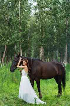 草地上穿婚纱的漂亮女人牵着马
