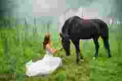 草地上穿婚纱的青年女人和马