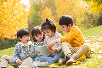 四个小朋友坐在草地上看平板电脑