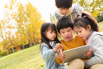 四个小朋友坐在草地上看平板电脑休闲活动高清镜头
