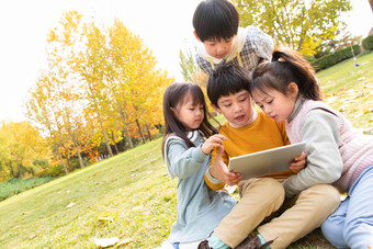 四个小朋友坐在草地上看平板<strong>电脑</strong>