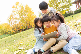 四个小朋友坐在草地上看平板电脑