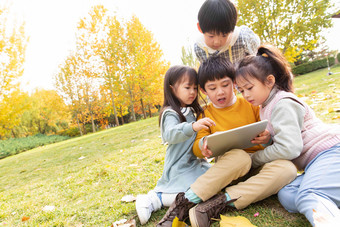 四个小朋友坐在草地上看平板电脑休闲活动清晰素材