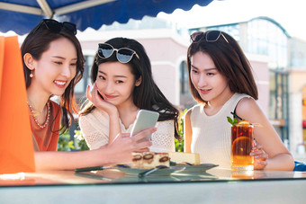 年轻女孩们坐在露天咖啡馆使用手机
