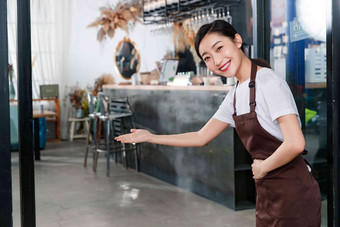 站着咖啡店门口做欢迎手势的女服务员