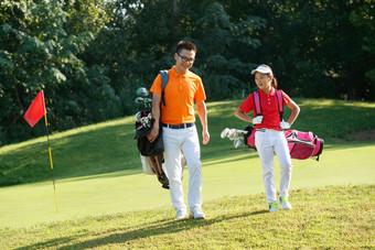 球场上教练和学生背着高尔夫球包行走植物繁盛高端相片