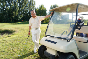快乐的老年人拿着球杆站在高尔夫球车旁
