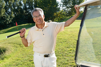 快乐的老年人扛着球杆站在高尔夫球车旁