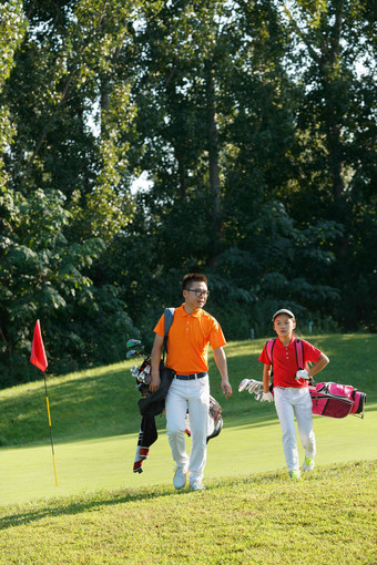 球场上教练和学生背着高尔夫球包行走绿色图片