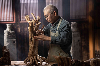 在树根上认真雕刻的工匠师中国镜头