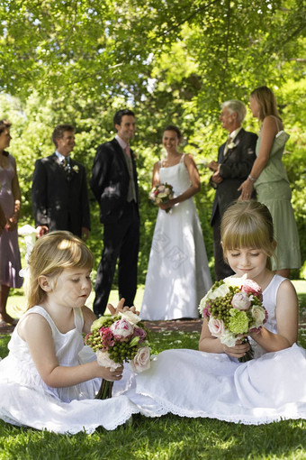 年轻的女孩坐着草坪上持有花束新娘新郎背景