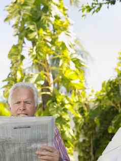 放松成熟的男人。阅读报纸植物在户外