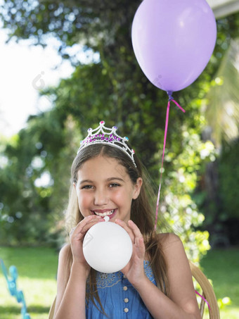 肖像微笑年轻的女孩穿头饰吹气球生日聚会，派对
