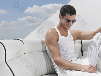 快乐年轻的男人。穿太阳镜放松沙发奢侈品游艇